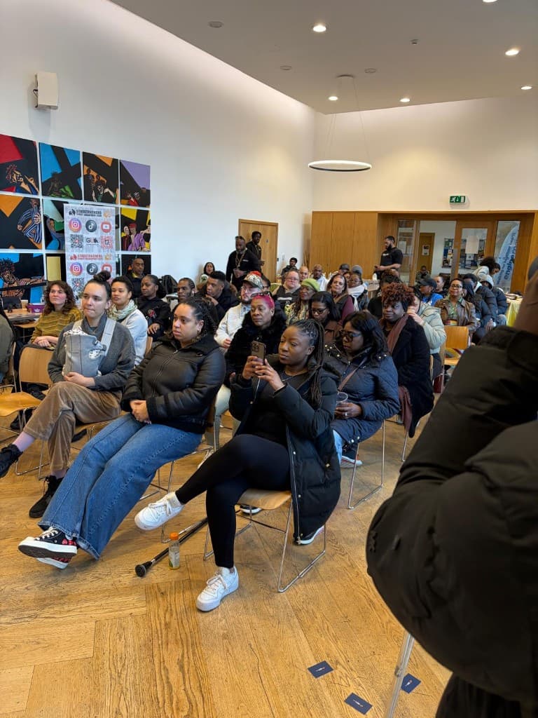 A diverse community seated together at an indoor event, listening attentively