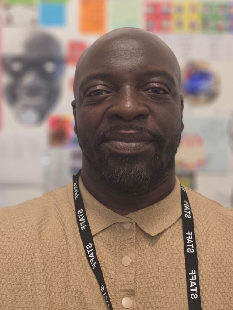Hakeem, assistant principal, wearing a tan polo shirt and a staff lanyard, smiling in a school setting.